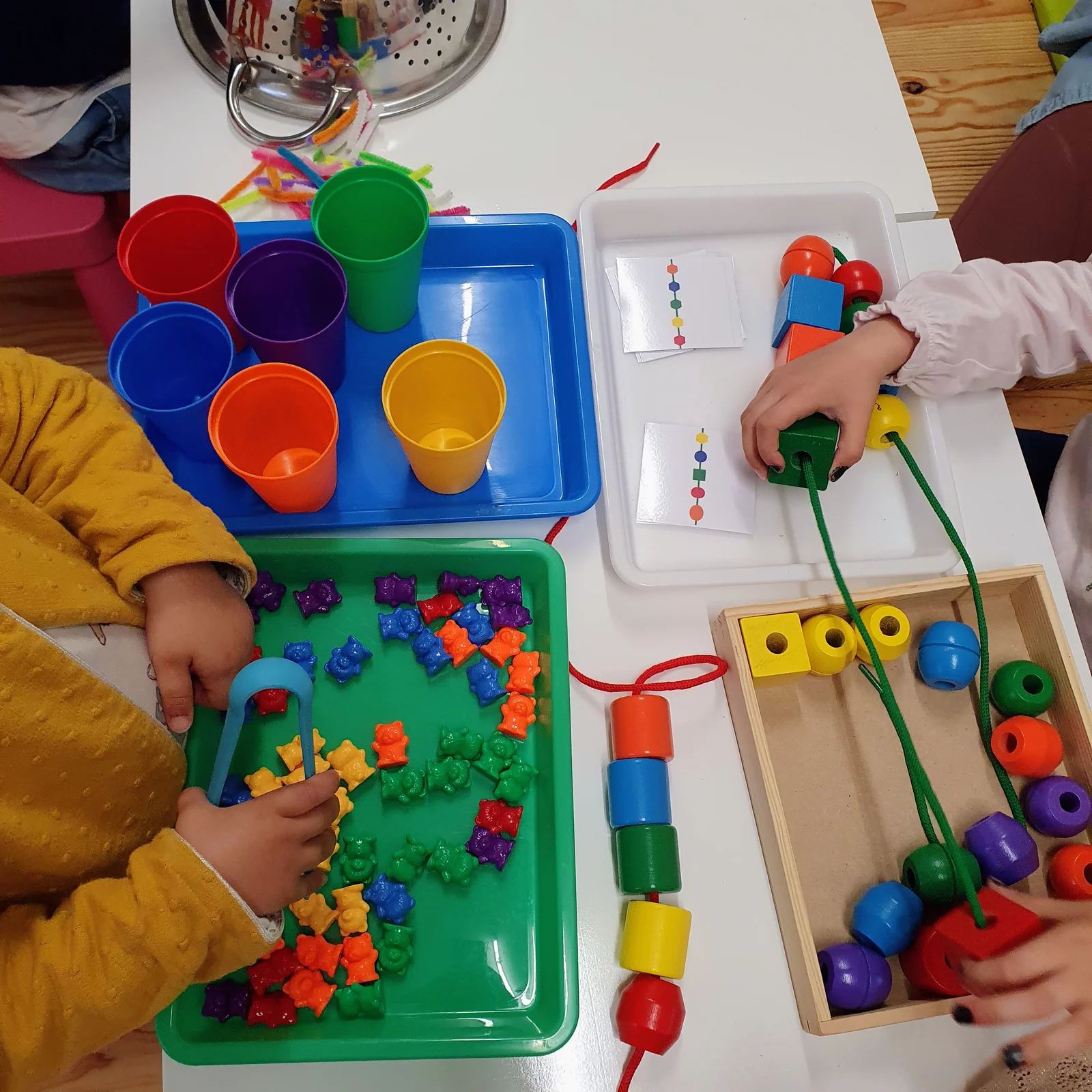 Plateaux d'activités motricité fine : tri d'oursons colorés à la pince, enfilage de perles en bois et séquences logiques
